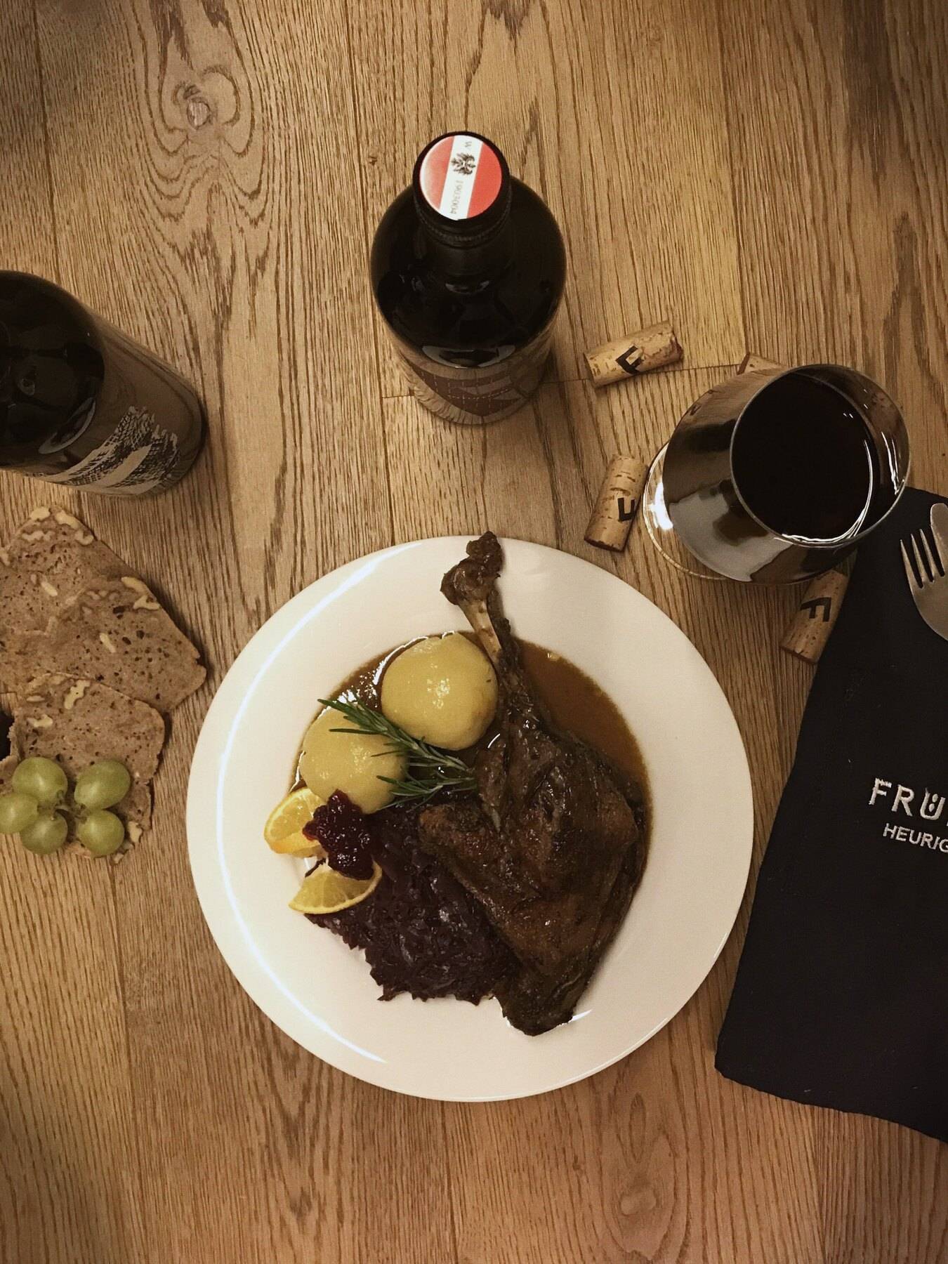 Der Gansl-Teller auf dem Holztisch mit Kürbis, Brot, Trauben und zwei Flaschen Rotwein