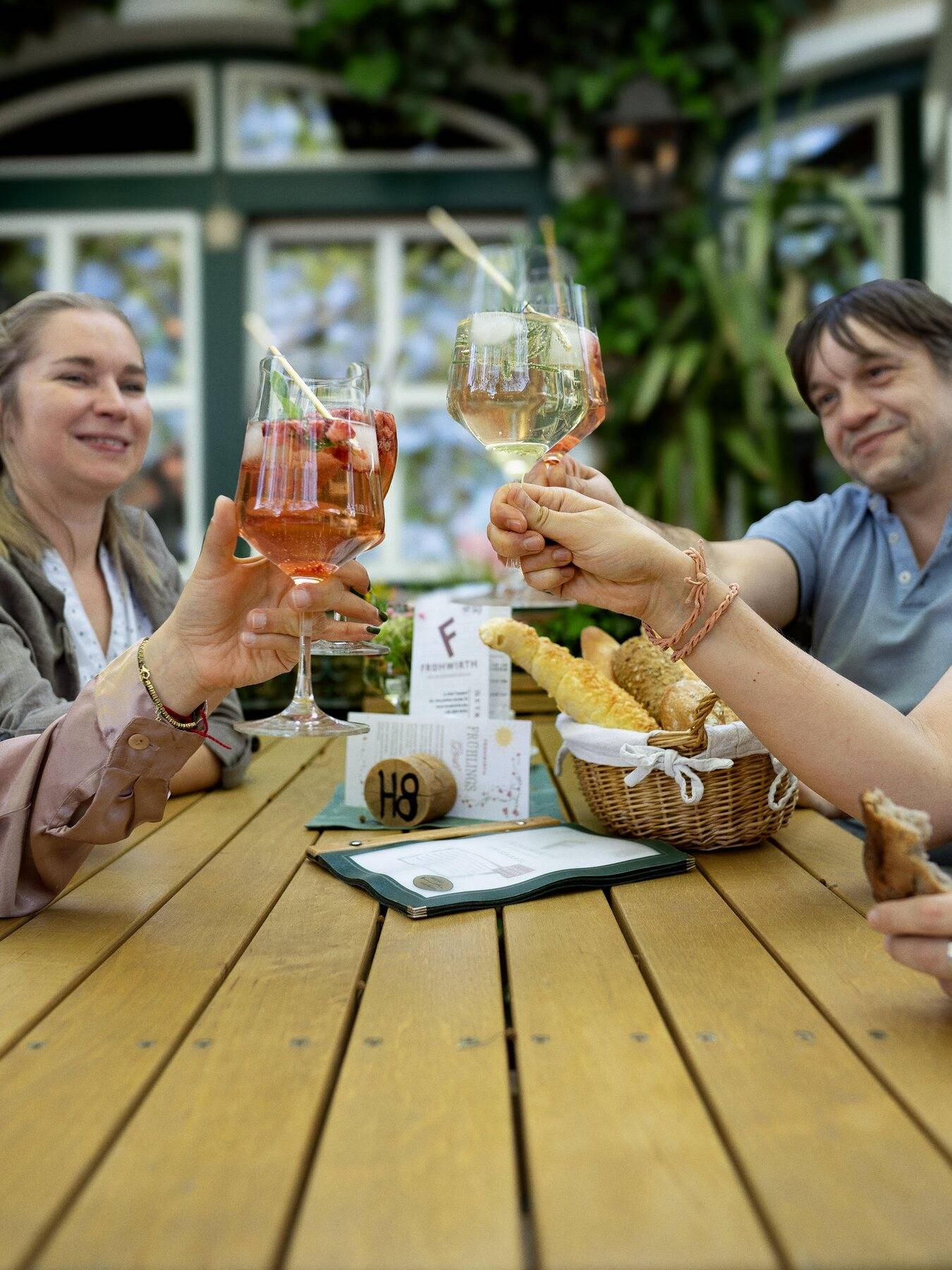 Vier Gäste stoßen im Gastgarten des Heurigen mit Spritzer und Wein an