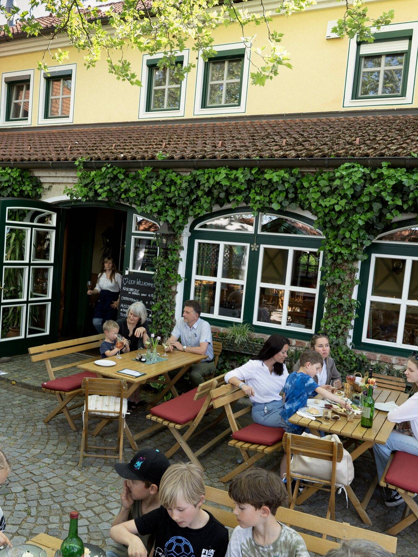 Der volle Gastgarten unter den Platanen vor dem efeubewachsenen Heurigenhaus