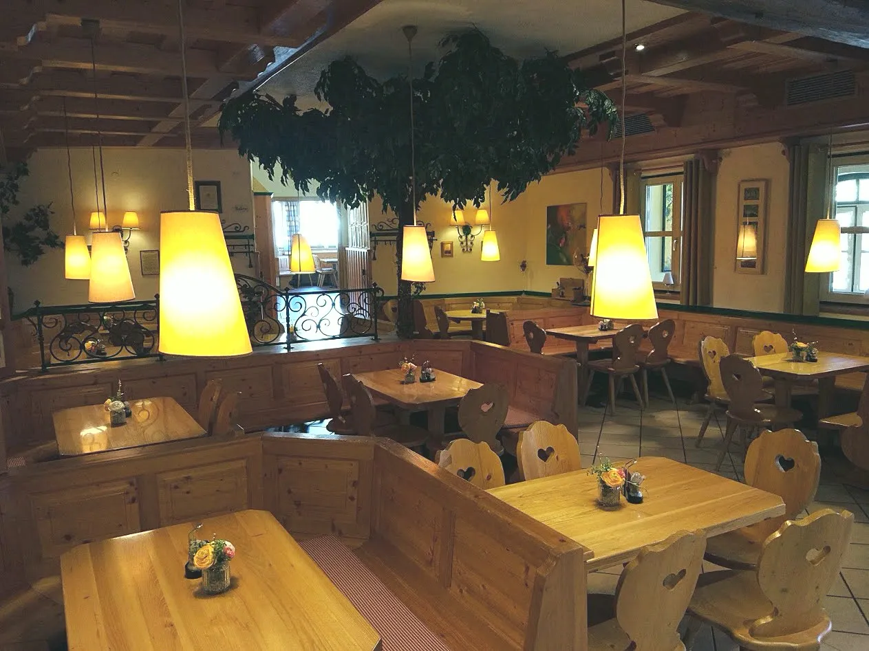 Holzvertäfelte Heurigenstube mit Herzerlstühlen, Holztischen, warmen Lampen und Föhrenzweig an der Decke