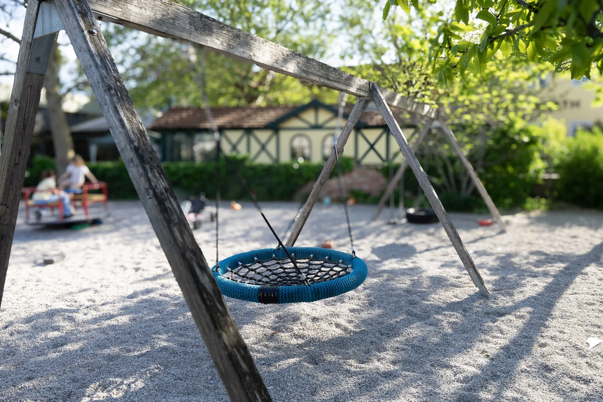 Kinderspielplatz mit Nestschaukel unter Bäumen im Gastgarten