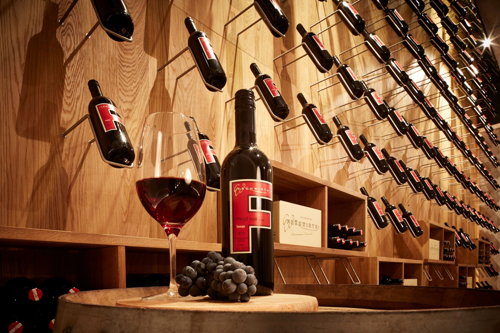 Ein Glas Rotwein und eine Flasche vor der Wand mit schräg gesteckten Flaschen