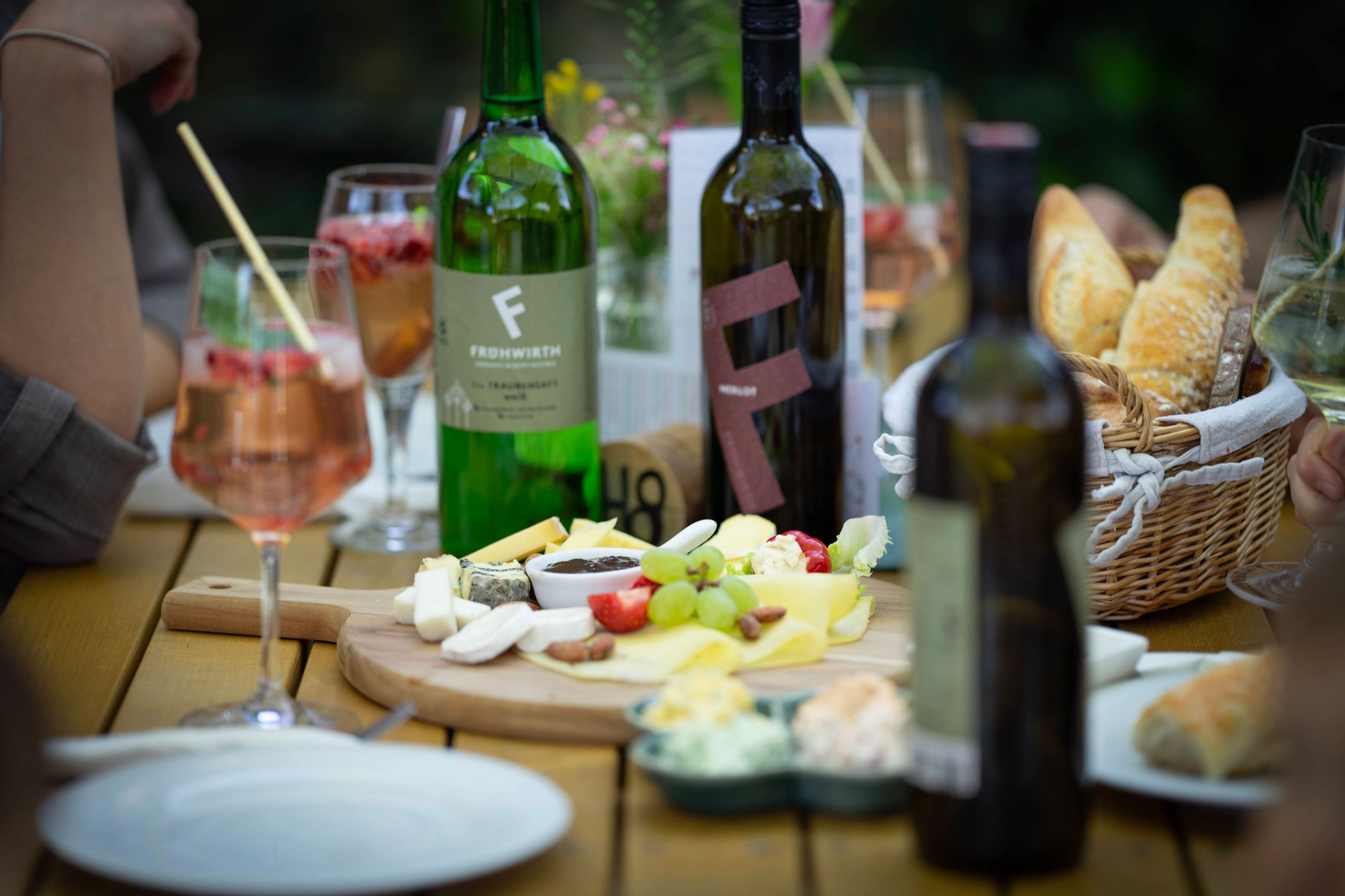 Gedeckter Heurigentisch mit Brettljause, Weinflaschen und Spritzer im Gastgarten