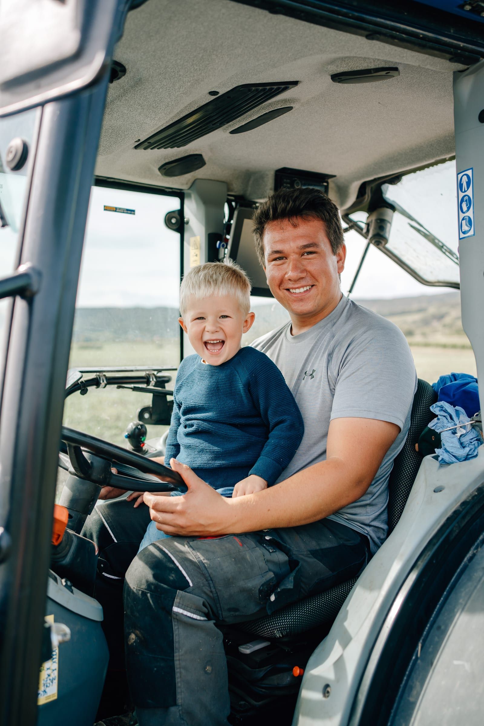 A winemaker sits at the wheel of the tractor with his little son